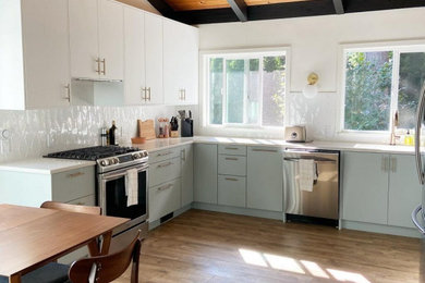 Inspiration for a mid-sized modern l-shaped laminate floor, brown floor and exposed beam eat-in kitchen remodel in Portland with an undermount sink, flat-panel cabinets, white cabinets, white backsplash, porcelain backsplash, stainless steel appliances, no island and white countertops