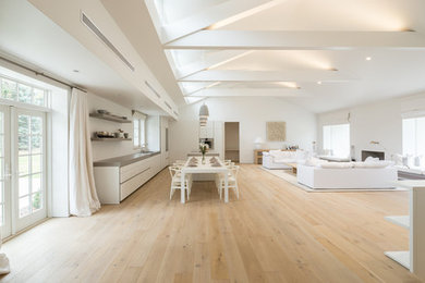 This is an example of a large modern l-shaped open plan kitchen in Philadelphia with flat-panel cabinets, white cabinets, panelled appliances, light hardwood floors and with island.