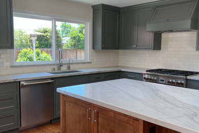L-shaped medium tone wood floor and brown floor kitchen photo in San Francisco with an undermount sink, green cabinets, quartz countertops, white backsplash, stainless steel appliances, an island and white countertops