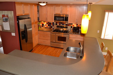 Inspiration for a small transitional l-shaped medium tone wood floor open concept kitchen remodel in Denver with an undermount sink, shaker cabinets, light wood cabinets, solid surface countertops, multicolored backsplash, porcelain backsplash, stainless steel appliances and an island
