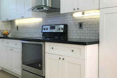Inspiration for a traditional u-shaped kitchen in Miami with light hardwood floors, grey floor, an undermount sink, shaker cabinets, white cabinets, granite benchtops, white splashback, ceramic splashback and stainless steel appliances.