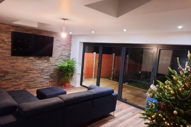 Photo of a large contemporary formal open plan living room feature wall in Essex with multi-coloured walls, laminate floors, a wall mounted tv and brown floors.