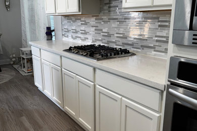 Kitchen - mid-sized traditional galley kitchen idea in Austin with shaker cabinets, white cabinets, quartzite countertops, multicolored backsplash, an island and white countertops