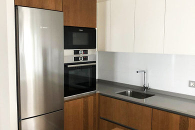 Imagen de cocinas en L minimalista de tamaño medio cerrada con fregadero de un seno, armarios con paneles lisos, puertas de armario de madera oscura, electrodomésticos de acero inoxidable, suelo de madera en tonos medios, una isla, suelo marrón y encimeras grises