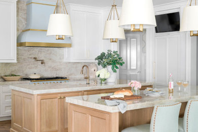 Example of a transitional u-shaped medium tone wood floor and brown floor kitchen design in Atlanta with two islands, an undermount sink, recessed-panel cabinets, white cabinets, marble countertops, beige backsplash, marble backsplash, paneled appliances and beige countertops