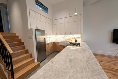 Example of a small minimalist u-shaped porcelain tile and gray floor eat-in kitchen design in New York with a farmhouse sink, flat-panel cabinets, white cabinets, quartzite countertops, white backsplash, quartz backsplash, stainless steel appliances, an island and gray countertops