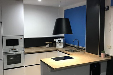 Modern inredning av ett litet kök, med en undermonterad diskho, släta luckor, vita skåp, vita vitvaror, klinkergolv i porslin, en halv köksö och grått golv