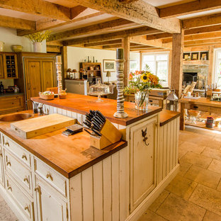 Mid-sized farmhouse kitchen pantry inspiration - Example of a mid-sized cottage l-shaped limestone floor kitchen pantry design in Burlington with a farmhouse sink, raised-panel cabinets, distressed cabinets, soapstone countertops, beige backsplash, subway tile backsplash, stainless steel appliances and an island