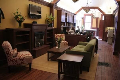 Modelo de despacho de estilo americano de tamaño medio con paredes amarillas, suelo de madera en tonos medios, todas las chimeneas, marco de chimenea de madera y escritorio independiente
