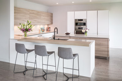 Inspiration for a mid-sized scandinavian u-shaped laminate floor and gray floor open concept kitchen remodel in Atlanta with an undermount sink, flat-panel cabinets, white cabinets, laminate countertops, gray backsplash, quartz backsplash, stainless steel appliances, two islands and gray countertops