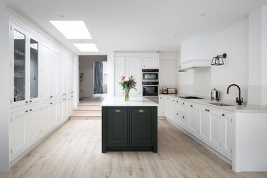 Large transitional l-shaped separate kitchen in London with a drop-in sink, shaker cabinets, marble benchtops, white splashback, marble splashback, stainless steel appliances, light hardwood floors, with island, beige floor and white benchtop.