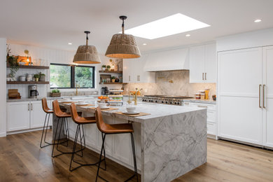 This is an example of a large transitional l-shaped kitchen in Los Angeles with an undermount sink, shaker cabinets, white cabinets, grey splashback, panelled appliances, light hardwood floors, with island, beige floor and grey benchtop.