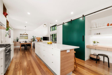 Modern galley kitchen pantry in Melbourne with white cabinets, quartz benchtops, white splashback, ceramic splashback, stainless steel appliances, light hardwood floors, with island and beige benchtop.