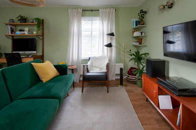 Foto de salón con barra de bar cerrado moderno de tamaño medio con paredes verdes, suelo laminado y televisor colgado en la pared