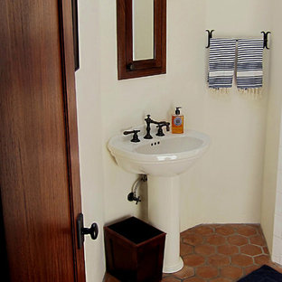 Small tuscan master terra-cotta tile and white tile terra-cotta floor and red floor corner shower photo in Santa Barbara with a two-piece toilet, white walls, a pedestal sink, open cabinets, medium tone wood cabinets and white countertops