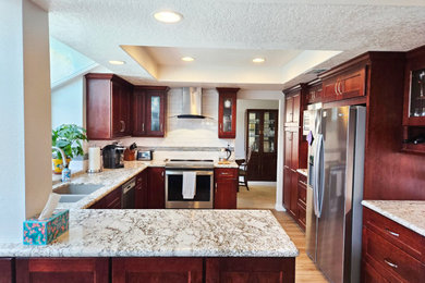 Example of a mid-sized transitional u-shaped vinyl floor, beige floor and coffered ceiling eat-in kitchen design in San Diego with an undermount sink, shaker cabinets, medium tone wood cabinets, granite countertops, white backsplash, ceramic backsplash, stainless steel appliances, a peninsula and beige countertops