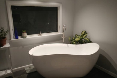 Diseño de cuarto de baño principal actual de tamaño medio con puertas de armario blancas, bañera exenta, paredes grises, encimera de acrílico, armarios con paneles empotrados y lavabo bajoencimera