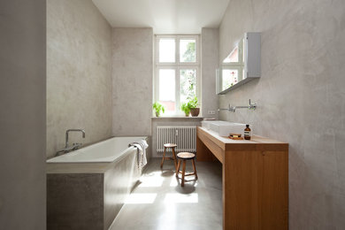Mittelgroßes Modernes Badezimmer mit Einbaubadewanne, grauer Wandfarbe, Betonboden, Aufsatzwaschbecken, Waschtisch aus Holz und brauner Waschtischplatte in Berlin