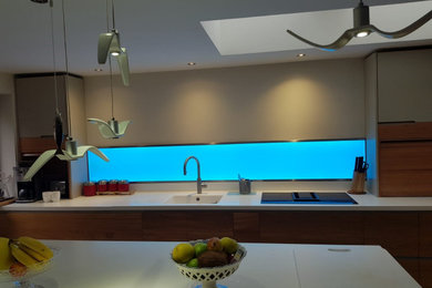 Inspiration for a medium sized contemporary single-wall kitchen/diner in Other with flat-panel cabinets, light wood cabinets, composite countertops, multi-coloured splashback, glass tiled splashback, an island and white worktops.