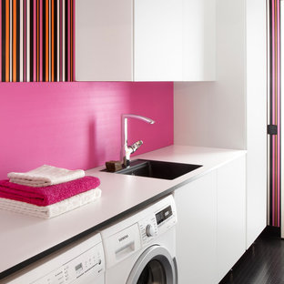 Inspiration for a medium sized contemporary single-wall separated utility room in Orebro with a single-bowl sink, flat-panel cabinets, white cabinets, pink walls, a side by side washer and dryer, laminate countertops and black floors.