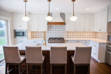 Example of a mid-sized transitional medium tone wood floor and brown floor kitchen design in Chicago with an undermount sink, recessed-panel cabinets, quartz countertops, mosaic tile backsplash, stainless steel appliances and an island