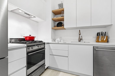Mid-sized transitional l-shaped separate kitchen in Chicago with an undermount sink, flat-panel cabinets, white cabinets, marble benchtops, white splashback, subway tile splashback, stainless steel appliances, light hardwood floors, no island and white benchtop.