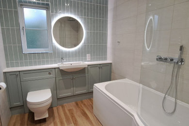 Inspiration for a medium sized contemporary family bathroom in Oxfordshire with shaker cabinets, blue cabinets, a corner bath, a shower/bath combination, a wall mounted toilet, grey tiles, porcelain tiles, wood-effect flooring, a built-in sink, solid surface worktops, a hinged door, white worktops, a single sink and a built in vanity unit.