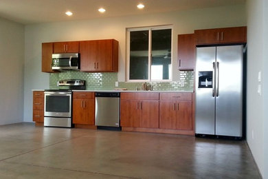 Inspiration for a mid-sized timeless single-wall concrete floor eat-in kitchen remodel in Hawaii with flat-panel cabinets, dark wood cabinets, solid surface countertops, green backsplash, porcelain backsplash, stainless steel appliances and no island