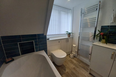 Design ideas for a medium sized modern family bathroom in Berkshire with flat-panel cabinets, white cabinets, a corner bath, a walk-in shower, a wall mounted toilet, blue tiles, porcelain tiles, white walls, porcelain flooring, a built-in sink, brown floors, a sliding door, white worktops, a wall niche, a single sink, a built in vanity unit and a drop ceiling.