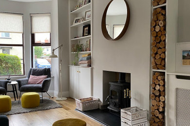 Modelo de salón nórdico de tamaño medio con paredes grises, suelo de madera clara, estufa de leña y pared multimedia