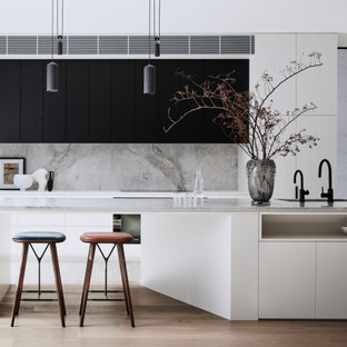Inspiration for a large contemporary l-shaped open plan kitchen in Sydney with a double-bowl sink, flat-panel cabinets, white cabinets, marble benchtops, grey splashback, marble splashback, black appliances, medium hardwood floors, with island, brown floor and grey benchtop.