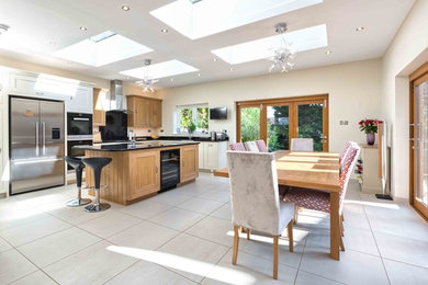 Design ideas for a large traditional l-shaped kitchen/diner in Hertfordshire with recessed-panel cabinets, light wood cabinets, stainless steel appliances, ceramic flooring and an island.