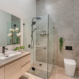 Foto di una stanza da bagno con doccia moderna con ante lisce, ante in legno chiaro, doccia ad angolo, WC monopezzo, piastrelle grigie, pareti bianche, lavabo da incasso, pavimento beige, porta doccia a battente e top beige