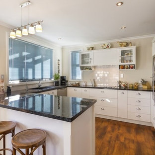 Mid-sized farmhouse kitchen pantry remodeling - Example of a mid-sized farmhouse u-shaped kitchen pantry design in Dunedin with flat-panel cabinets, white cabinets, laminate countertops, white backsplash, ceramic backsplash, stainless steel appliances and an island