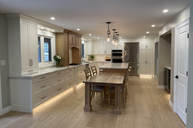 Example of a transitional light wood floor kitchen design in Toronto with an undermount sink, shaker cabinets, quartz countertops, white backsplash, porcelain backsplash, stainless steel appliances and an island