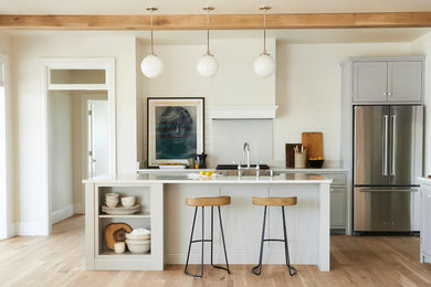 Example of a mid-sized transitional l-shaped light wood floor and brown floor open concept kitchen design in Other with shaker cabinets, gray cabinets, white backsplash, subway tile backsplash, stainless steel appliances and an island