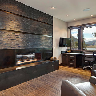 Inspiration for a medium sized modern home office and library in Denver with white walls, medium hardwood flooring, a two-sided fireplace, a stone fireplace surround, a built-in desk and brown floors.