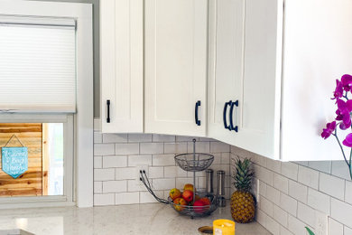 Inspiration for a contemporary l-shaped kitchen remodel in Grand Rapids with a single-bowl sink, shaker cabinets, white cabinets, quartz countertops, white backsplash, subway tile backsplash, an island and white countertops