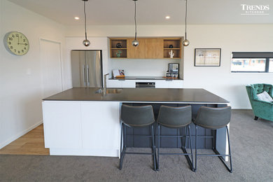 Design ideas for a modern kitchen in Christchurch with white cabinets, solid surface benchtops, stainless steel appliances, laminate floors, with island, brown floor and black benchtop.