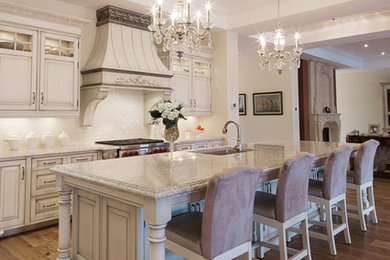 Large elegant single-wall medium tone wood floor and beige floor eat-in kitchen photo in Toronto with raised-panel cabinets, distressed cabinets, granite countertops, stainless steel appliances and an island