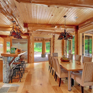 Cette photo montre une grande salle à manger ouverte sur la cuisine montagne avec un mur marron, un sol en bois clair et aucune cheminée.