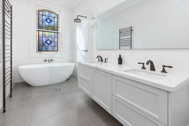 Bathroom - mid-sized transitional master white tile and subway tile porcelain tile, gray floor and double-sink bathroom idea in Melbourne with shaker cabinets, white cabinets, white walls, an undermount sink, quartz countertops, white countertops and a floating vanity