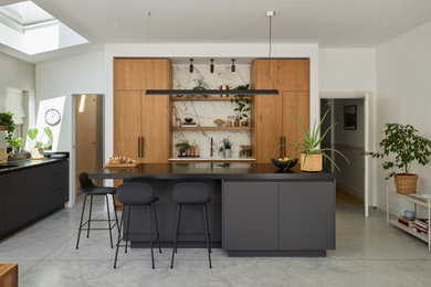 This is an example of a large contemporary kitchen/diner in London with a single-bowl sink, flat-panel cabinets, medium wood cabinets, granite worktops, multi-coloured splashback, marble splashback, concrete flooring, an island, grey floors, black worktops, feature lighting and integrated appliances.