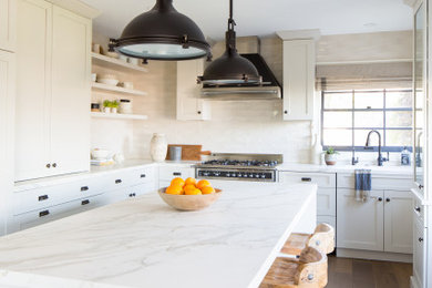 Eat-in kitchen - mid-sized country u-shaped medium tone wood floor and beige floor eat-in kitchen idea in Orange County with an undermount sink, shaker cabinets, white cabinets, solid surface countertops, beige backsplash, ceramic backsplash, paneled appliances, an island and white countertops