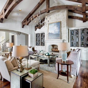 Ejemplo de salón para visitas abierto, mediterráneo, grande, con paredes beige, suelo de madera oscura, chimenea tradicional, marco de chimenea de yeso, televisor retractable y suelo marrón