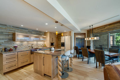 Inspiration for a mid-sized contemporary l-shaped light wood floor and beige floor open concept kitchen remodel in Denver with a farmhouse sink, shaker cabinets, light wood cabinets, granite countertops, beige backsplash, stone tile backsplash, stainless steel appliances and an island