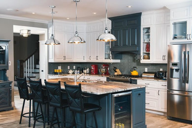 Example of a large arts and crafts l-shaped kitchen design in Other with an undermount sink, raised-panel cabinets, white cabinets, granite countertops, gray backsplash, glass tile backsplash, stainless steel appliances and an island