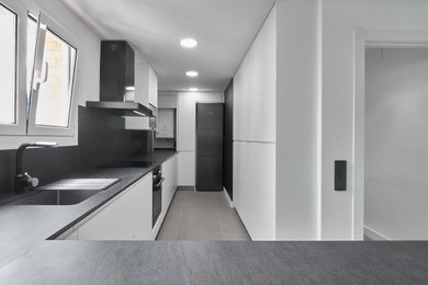 Medium sized modern grey and white open plan kitchen in Barcelona with a submerged sink, flat-panel cabinets, white cabinets, laminate countertops, ceramic flooring, a breakfast bar, grey floors and black worktops.
