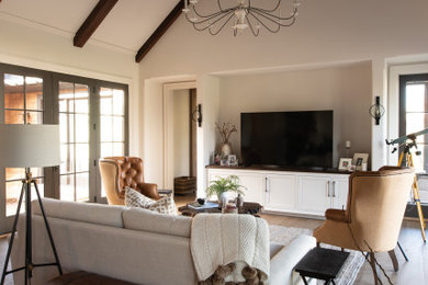 Ejemplo de salón abierto clásico grande con paredes beige, suelo de madera clara, pared multimedia y vigas vistas