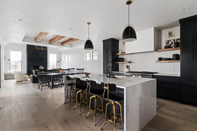 Mid-sized danish l-shaped light wood floor, beige floor and exposed beam open concept kitchen photo in Boise with an undermount sink, flat-panel cabinets, black cabinets, quartzite countertops, white backsplash, subway tile backsplash, stainless steel appliances, an island and white countertops
